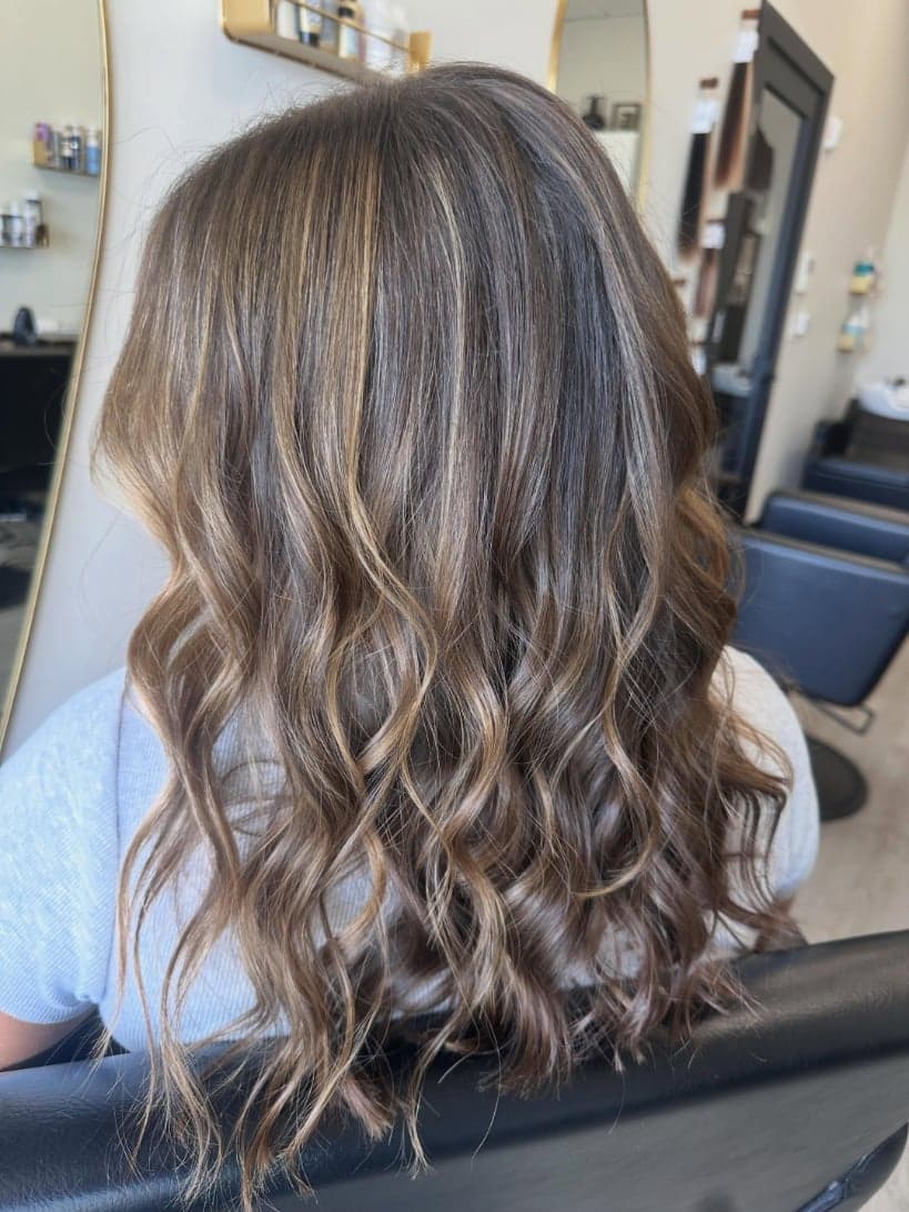 Warm caramel balayage through brunette waves, back view — hair by Alchemy Loft